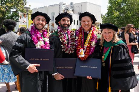 Four college graduates in their cap and gowns, holding their degrees