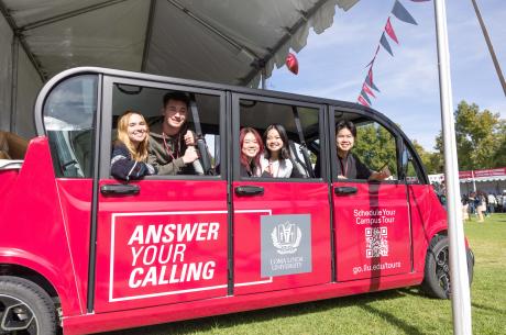 College students in a red, over-sized golf cart, smiling at the camera