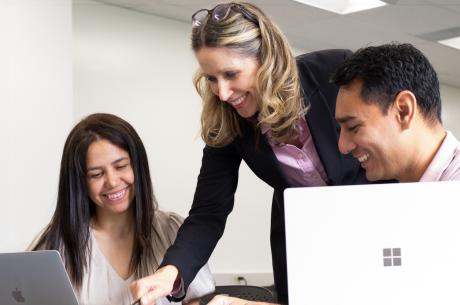 Female Caucasian teacher with male and female college student looking at computers.