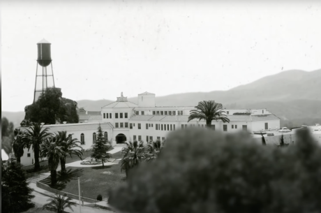 black and white photo of a university campus, hills in the background, trees in the foreground